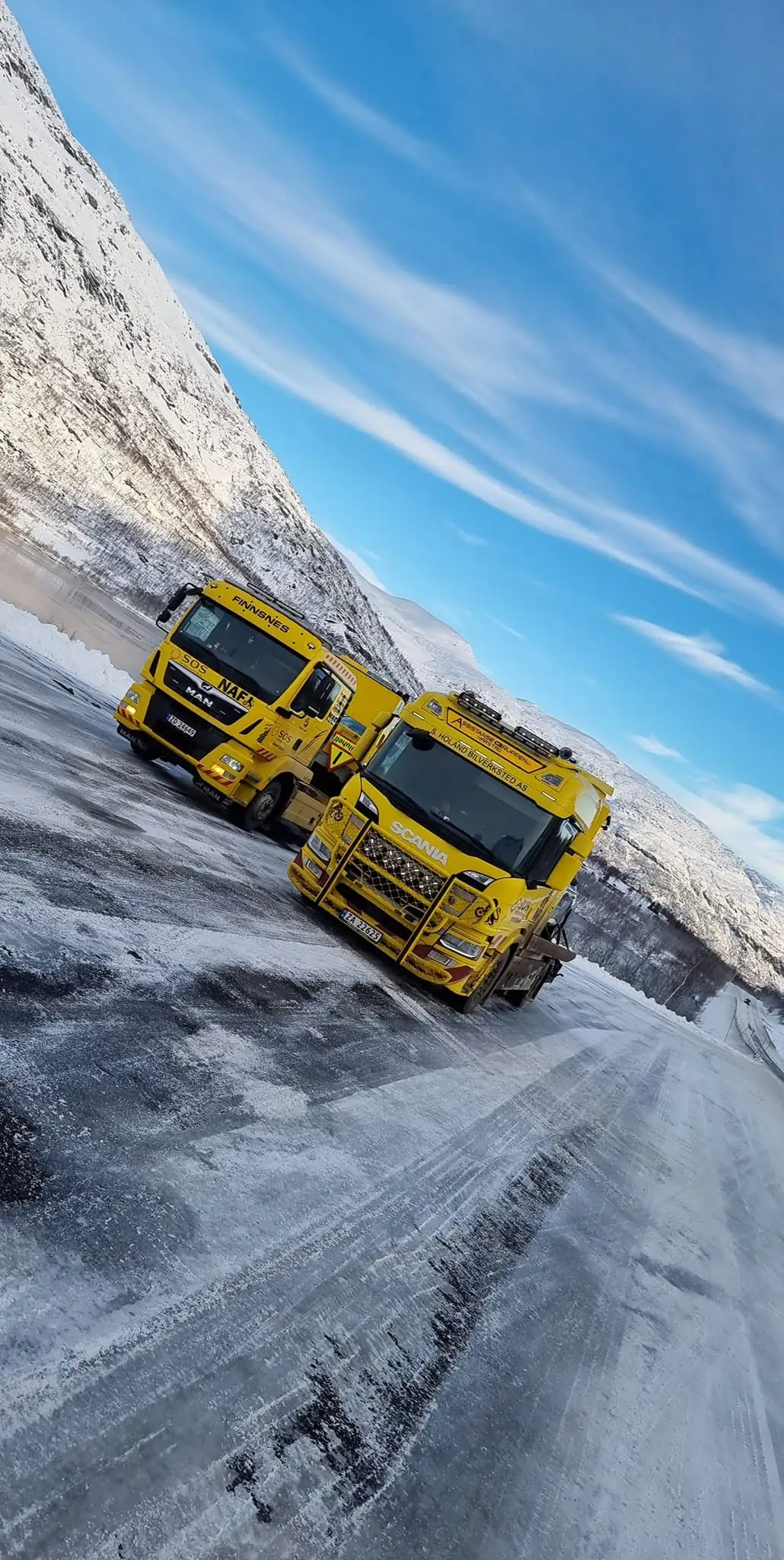 To gule bergingsbiler parkert på en snødekt fjellvei i vintersol