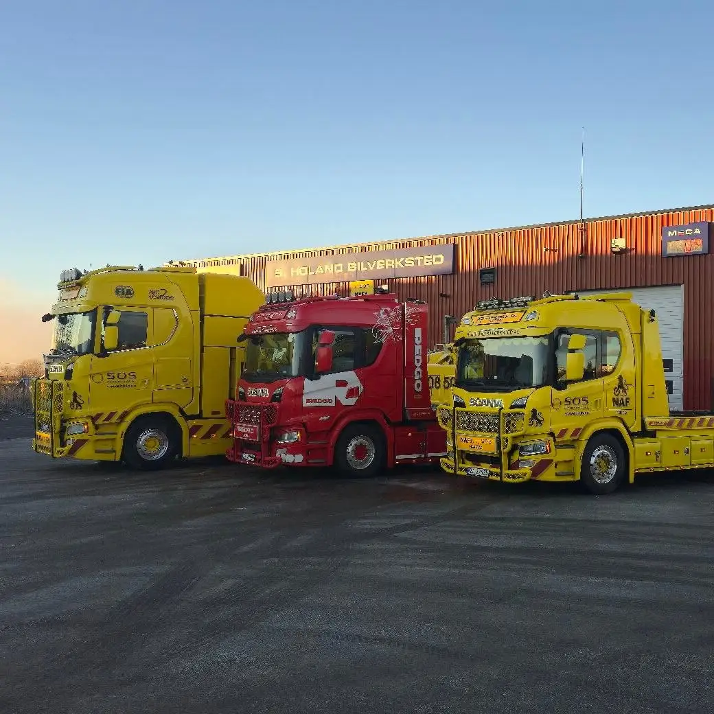 Tre bergingsbiler foran verkstedet med S. Holand Bilverksted-skiltet opplyst